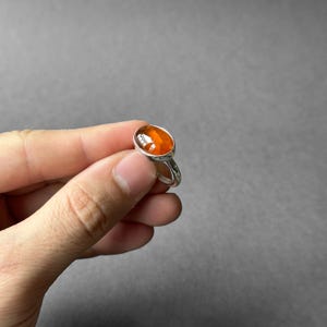 May include: A silver ring with an oval-shaped orange gemstone.