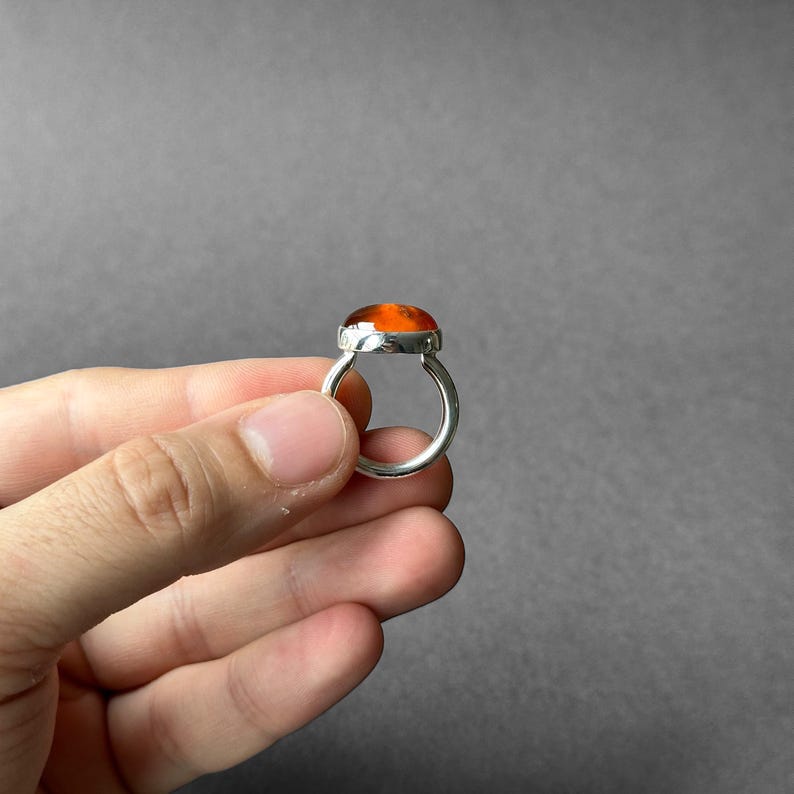 May include: A silver ring with an orange gemstone set in a bezel setting.