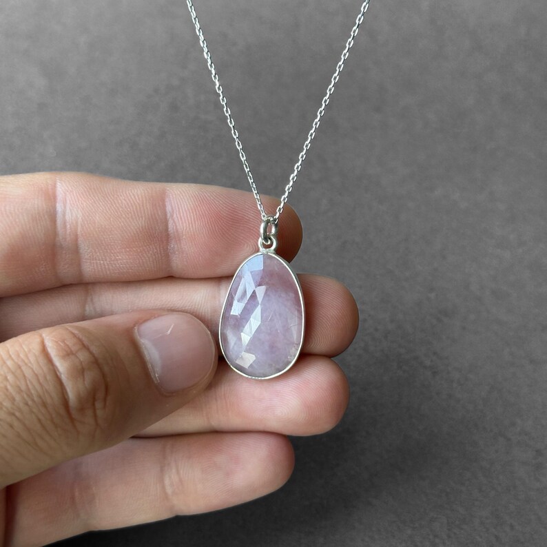 May include: A silver chain necklace with a light pink faceted gemstone pendant.