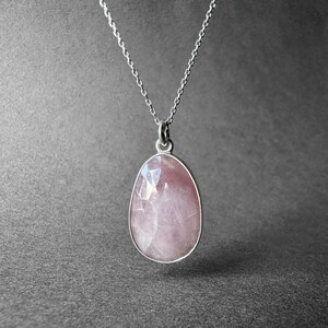 May include: A silver chain necklace with a pink rose quartz pendant. The pendant is oval shaped and has a faceted cut.