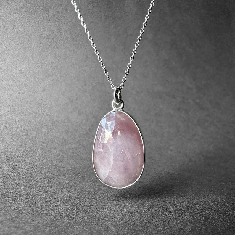 May include: A silver chain necklace with a pink rose quartz pendant. The pendant is oval shaped and has a faceted cut.