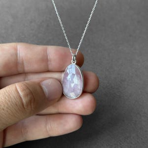 May include: A silver chain necklace with a light pink, faceted gemstone pendant.