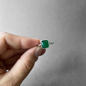 K&ouml;nnte beinhalten: Ein Silberring mit einem rechteckigen, smaragdgeschliffenen gr&uuml;nen Edelstein in einer glatten Zargenfassung. Das Band besteht aus poliertem Silber und der Stein hat eine tiefe, leuchtende gr&uuml;ne Farbe mit einer facettierten Oberfl&auml;che.