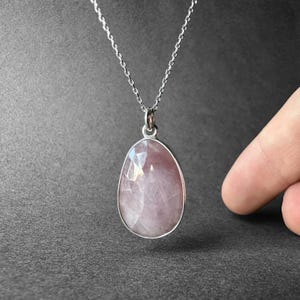 May include: A silver chain necklace with a pink oval gemstone pendant.