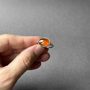 May include: A silver ring with an orange oval gemstone.