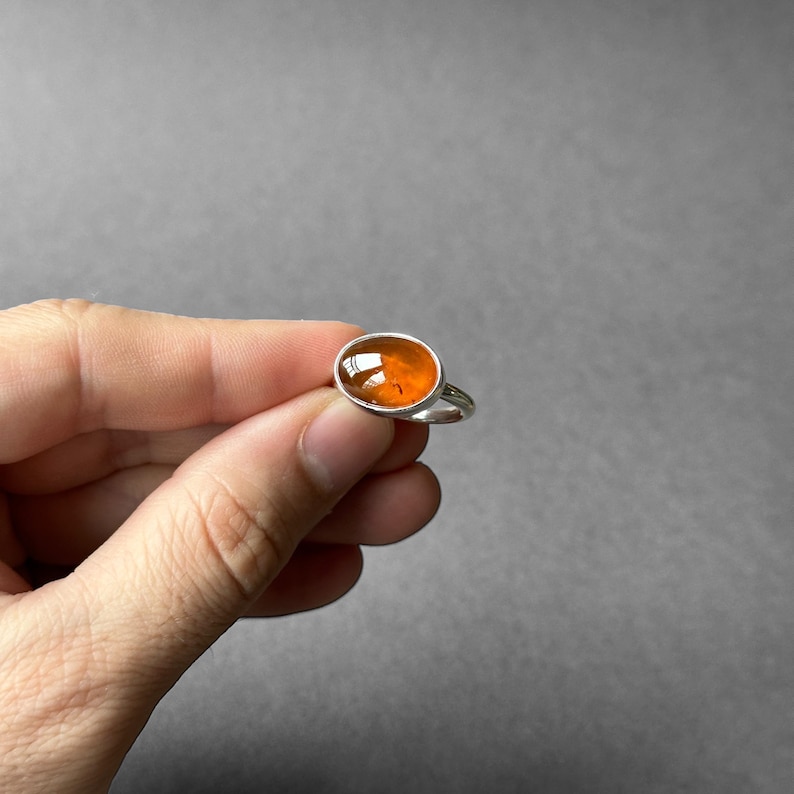 May include: A silver ring with an orange oval gemstone.