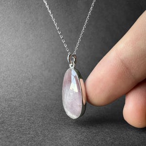 May include: A silver chain necklace with a pink rose quartz pendant. The pendant is oval shaped and has a smooth, polished finish.
