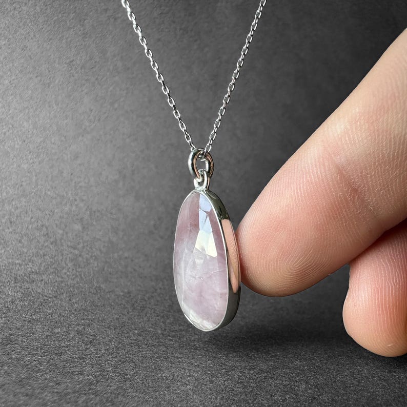 May include: A silver chain necklace with a pink rose quartz pendant. The pendant is oval shaped and has a smooth, polished finish.