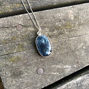 Peut inclure: Un collier en cha&icirc;ne argent avec un pendentif ovale bleu orn&eacute; d'une pierre textur&eacute;e scintillante.