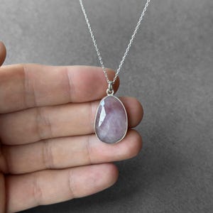 May include: A silver chain necklace with a pink gemstone pendant. The pendant is oval shaped and has a faceted cut.