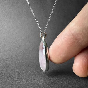 May include: A silver chain necklace with a pink oval gemstone pendant.