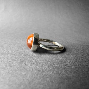 May include: A silver ring with a large, round, orange gemstone set in a bezel setting.