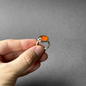 May include: A silver ring with an orange gemstone set in a bezel setting.