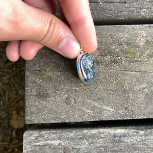 Peut inclure: Un pendentif en argent avec une pierre ovale gris fonc&eacute;. La pierre a un motif mouchet&eacute;.