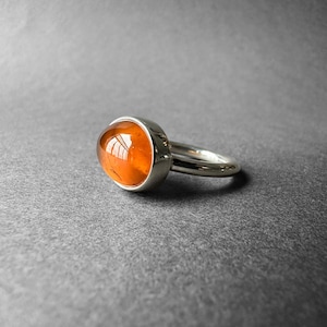 May include: A silver ring with an oval-shaped orange gemstone set in a bezel setting.