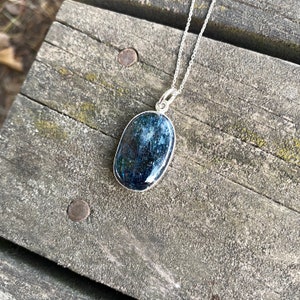 Peut inclure: Un collier en argent avec un pendentif ovale bleu fonc&eacute;. Le pendentif a une finition scintillante et iris&eacute;e.