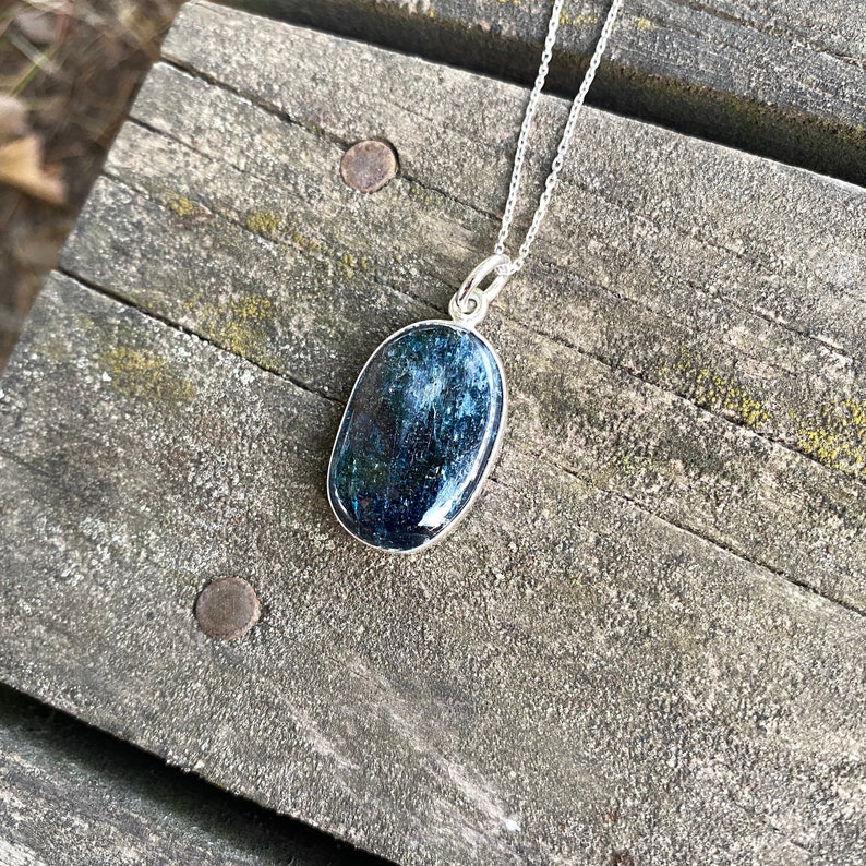 Peut inclure: Un collier en argent avec un pendentif ovale bleu fonc&eacute;. Le pendentif a une finition scintillante et iris&eacute;e.