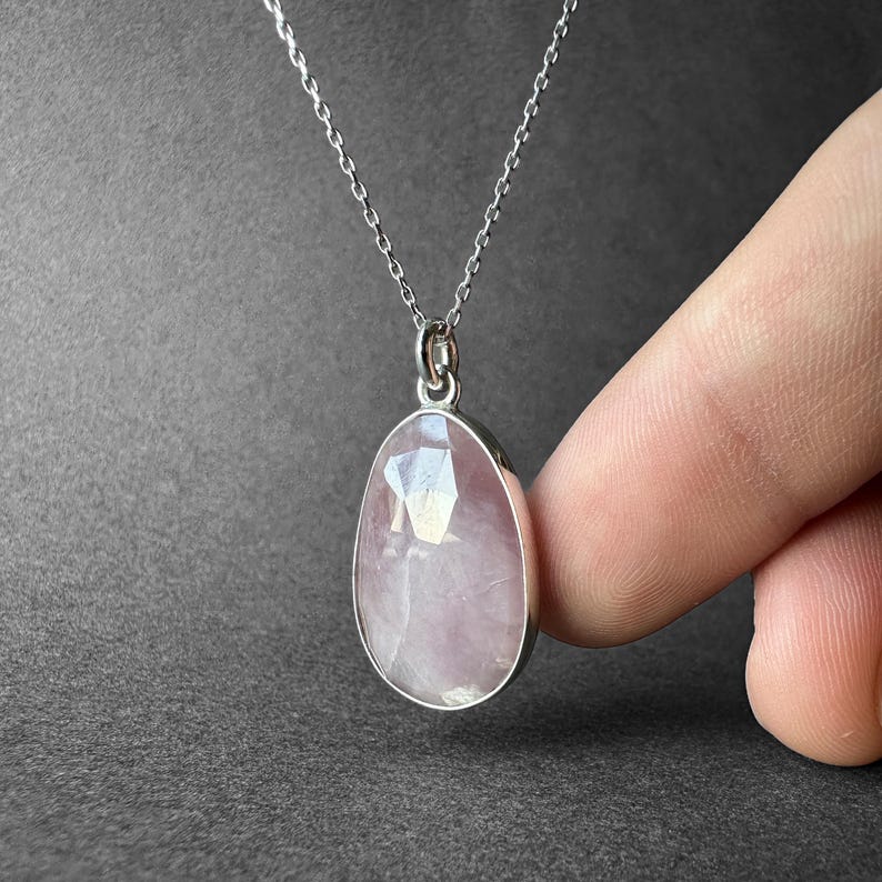 May include: A silver chain necklace with a pink oval-shaped gemstone pendant.