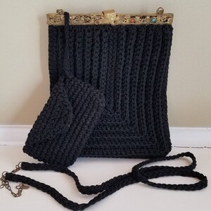 Puede incluir: Un bolso de crochet negro con un cierre de metal dorado y una correa de crochet negra a juego. El bolso tiene un peque&ntilde;o bolso de crochet a juego adjunto.