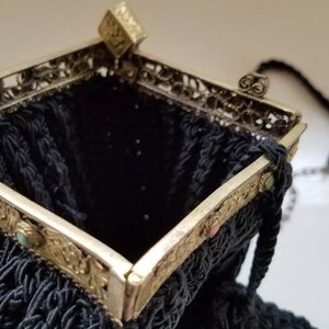 Puede incluir: Un bolso de noche negro de cuentas con un marco de metal plateado y detalles ornamentados. El bolso tiene una correa de cadena y un cierre de broche.