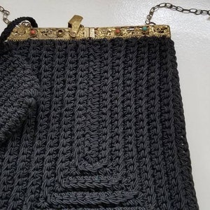 Puede incluir: Un bolso de crochet negro con cierre dorado y una peque&ntilde;a bolsa a juego. El bolso tiene una correa de cadena.