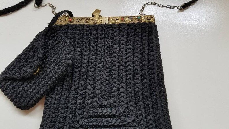 Puede incluir: Un bolso de crochet negro con cierre dorado y una peque&ntilde;a bolsa a juego. El bolso tiene una correa de cadena.