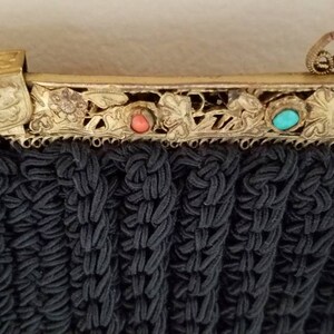 Puede incluir: Un bolso de noche negro de cuentas con un marco de metal dorado y detalles florales decorativos. El marco tiene tres piedras de color turquesa y coral.