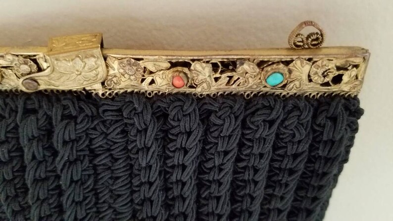 Puede incluir: Un bolso de noche negro de cuentas con un marco de metal dorado y detalles florales decorativos. El marco tiene tres piedras de color turquesa y coral.
