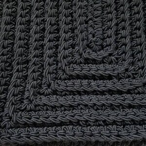 Puede incluir: Bolso de crochet negro con forma cuadrada y un patr&oacute;n texturizado.