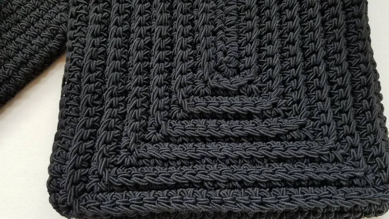 Puede incluir: Bolso de crochet negro con forma cuadrada y un patr&oacute;n texturizado.