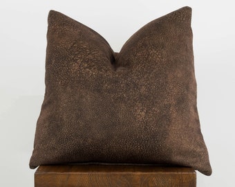 May include: A brown suede pillow with a textured surface sits on a wooden stool.