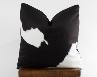 May include: Black and white cowhide patterned throw pillow on a wooden stool.