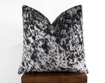May include: A black and white cowhide pillow sits on a wooden stool. The pillow has a soft, plush texture and a unique, natural pattern.