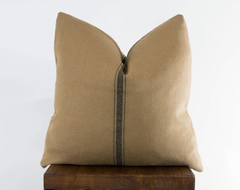 May include: A tan throw pillow with black stripes sits on a wooden stool. The pillow is made of a soft, textured fabric.