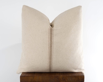 May include: A beige throw pillow with a brown stripe down the center, sitting on a wooden stool.