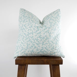 May include: A light blue throw pillow with a white floral pattern sits on a wooden stool.
