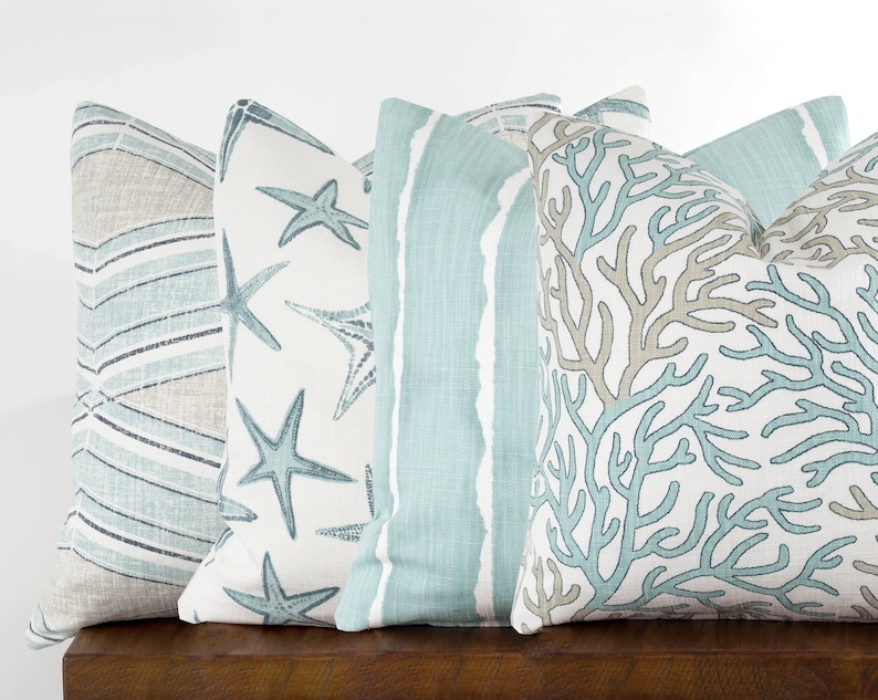 Puede incluir: Cuatro almohadas decorativas con tem&aacute;tica costera. Las almohadas presentan una variedad de patrones, incluyendo rayas, estrellas de mar y corales.