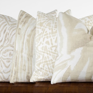 May include: Four decorative throw pillows with a beige linen fabric and abstract patterns in shades of beige and white.