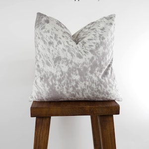 May include: A gray and white cowhide patterned throw pillow on a wooden stool. The pillow is labeled "Salt & Pepper Grey".