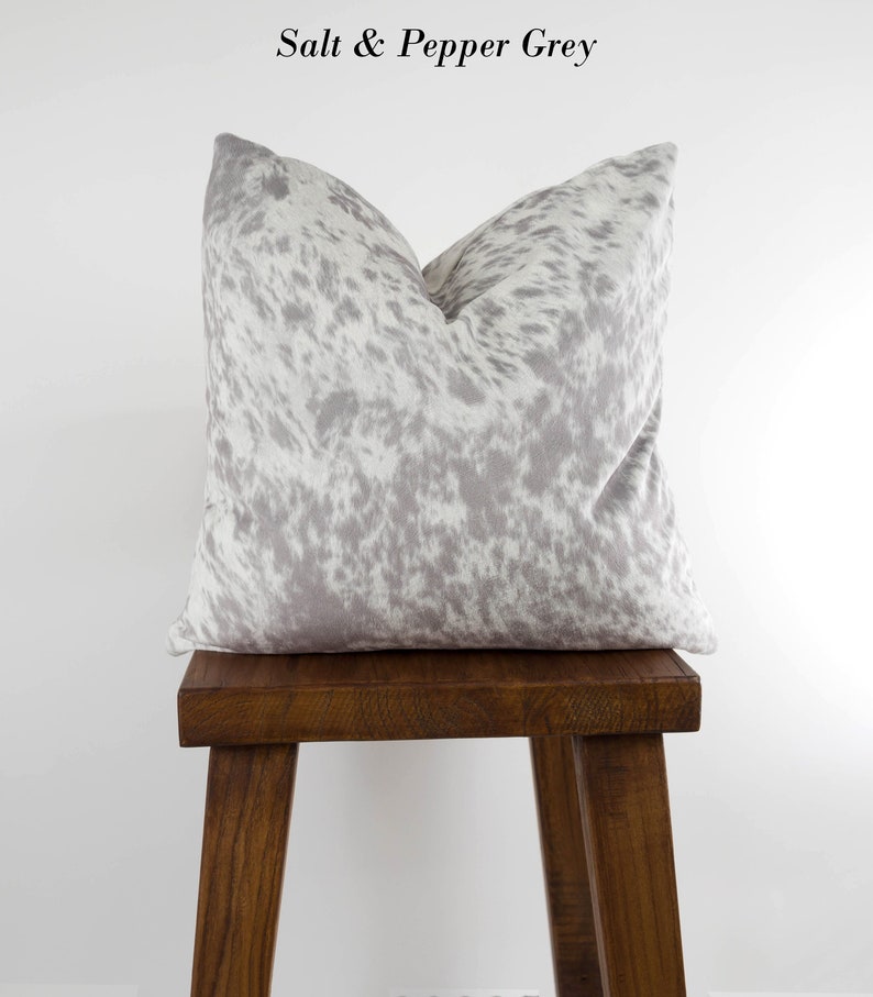 May include: A gray and white cowhide patterned throw pillow on a wooden stool. The pillow is labeled "Salt & Pepper Grey".