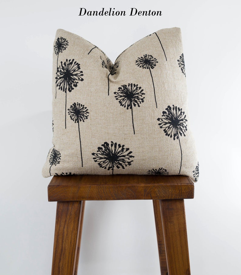 May include: A beige linen pillow with a black dandelion print. The pillow is sitting on a wooden stool.