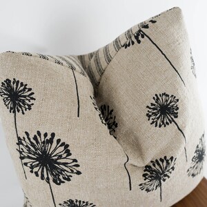 May include: Two beige linen throw pillows with a black dandelion print. The pillows are arranged in a V-shape.