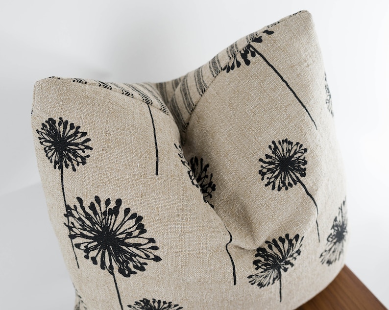 May include: Two beige linen throw pillows with a black dandelion print. The pillows are arranged in a V-shape.