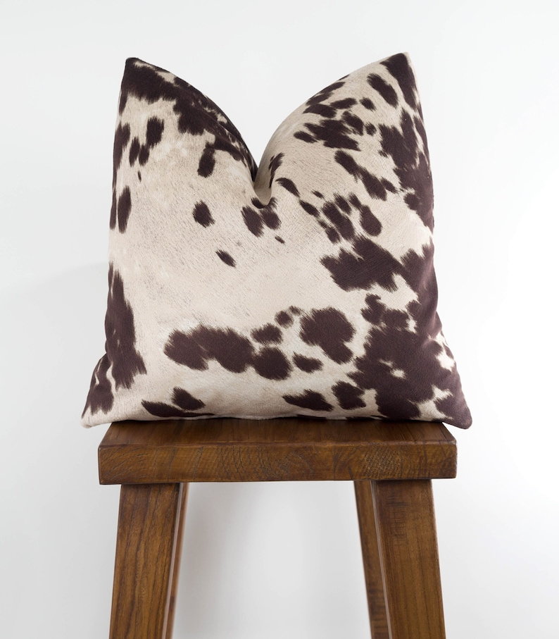 May include: A brown and white cowhide patterned throw pillow on a wooden stool.