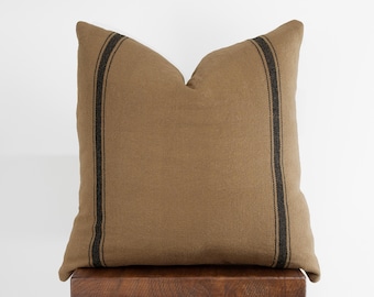 May include: A brown throw pillow with black stripes. The pillow is made of a textured fabric and has a simple, farmhouse style.