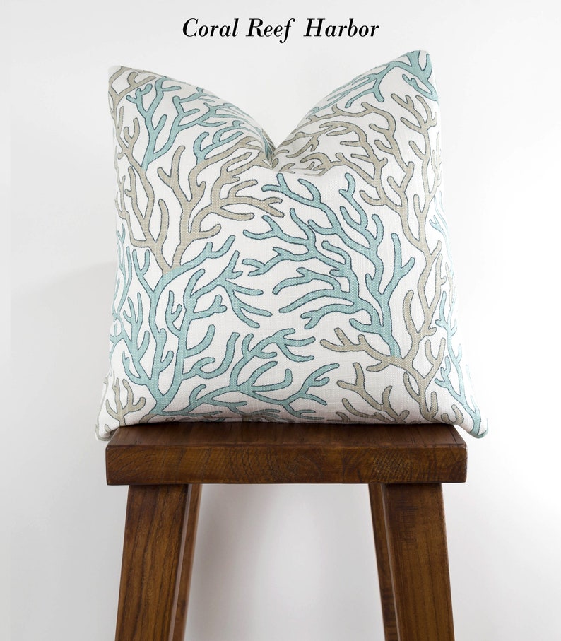 Puede incluir: Una almohada decorativa con un patr&oacute;n de arrecife de coral en tonos azules y beige. La almohada est&aacute; sentada en un taburete de madera.