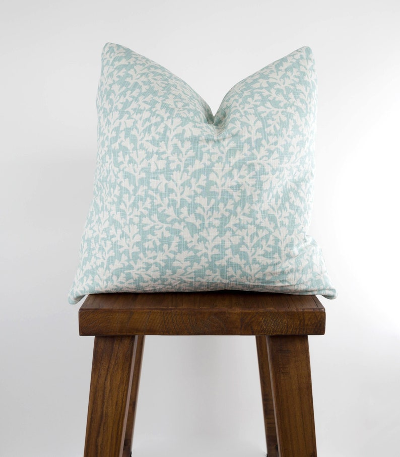 May include: A light blue throw pillow with a white floral pattern sits on a wooden stool.