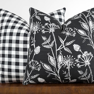 May include: Three decorative throw pillows with black and white patterns. The pillow on the left has a black and white gingham pattern. The middle pillow has a black background with a white floral pattern. The pillow on the right has a black background with a white floral pattern.