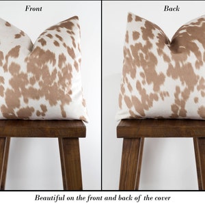 May include: A brown and white cowhide patterned pillow cover. The pattern is visible on both the front and back of the pillow cover.