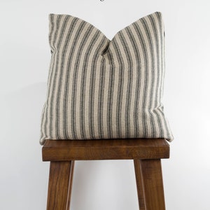 May include: A black and white striped pillow on a wooden stool. The pillow is made of ticking fabric and has a simple, farmhouse style.